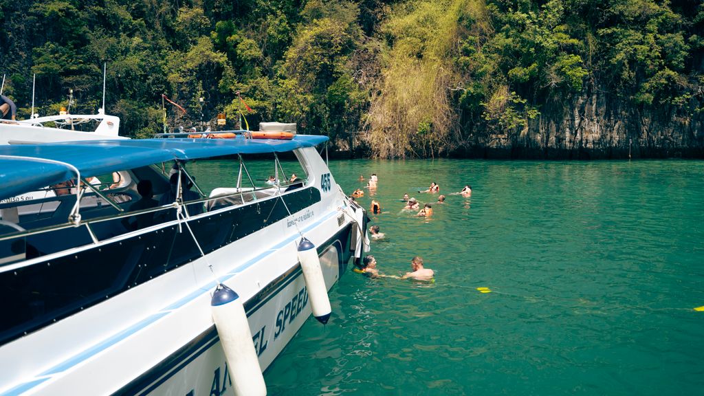 Group of tourists swimming in turquoise waters near a speedboat along the lush coastline of Thailand.